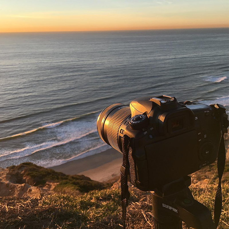 a dslr camera on a tripod aimed out over the ocean at sunset