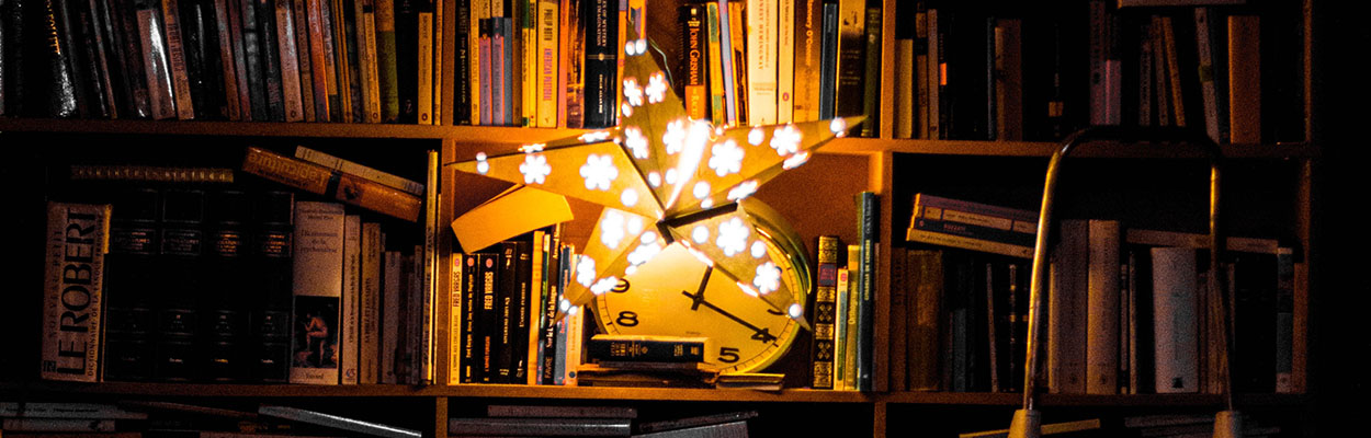 A bookshelf with a glowing fairy light star hanging from the shelf and illuminating the books